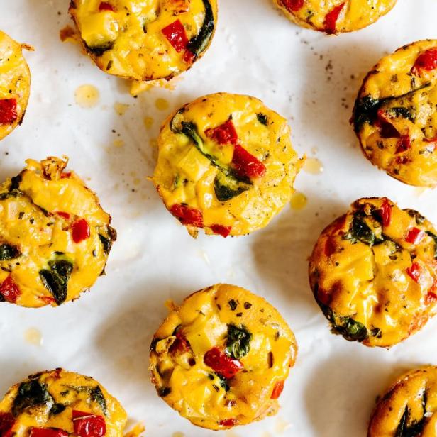 Mehrere Eier-Muffins mit Gemüse liegen auf einem weißen Untergrund.