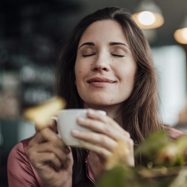 Eine lächelnde Geschäftsfrau riecht an ihrem Kaffee in einem Café.