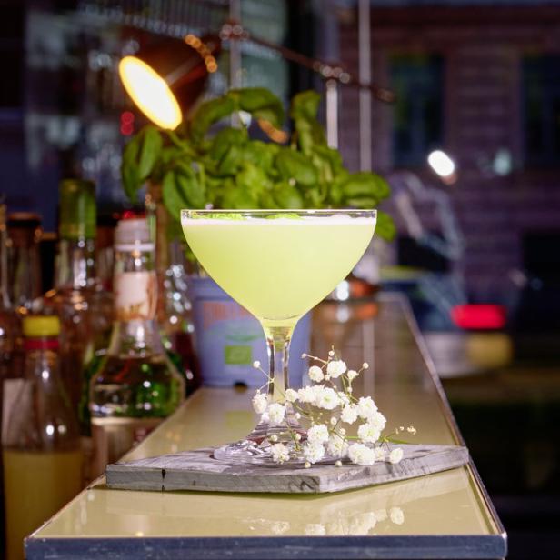 Ein hellgrüner Cocktail in einem Glas auf einer Bar, dekoriert mit Schleierkraut.