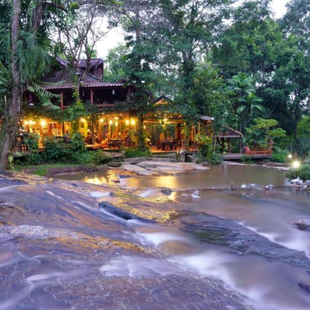 Ein Restaurant mit Außenbereich liegt an einem Fluss inmitten üppiger Vegetation.