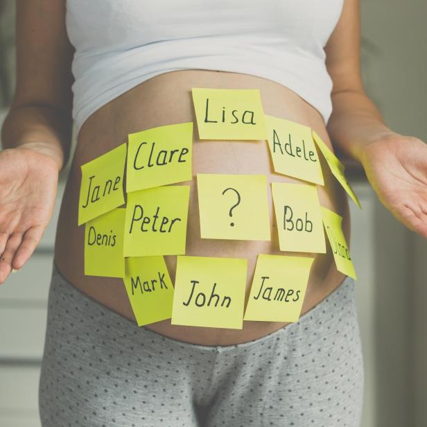 Eine schwangere Frau mit Zetteln mit Namen auf ihrem Bauch, die mögliche Babynamen darstellen.