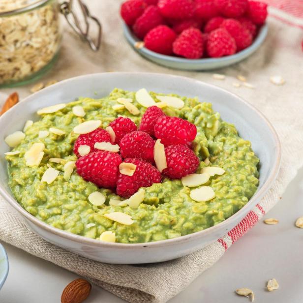 Haferflocken-Matcha-Brei mit frischen Himbeeren und Nüssen in einer Schüssel auf einer Serviette.