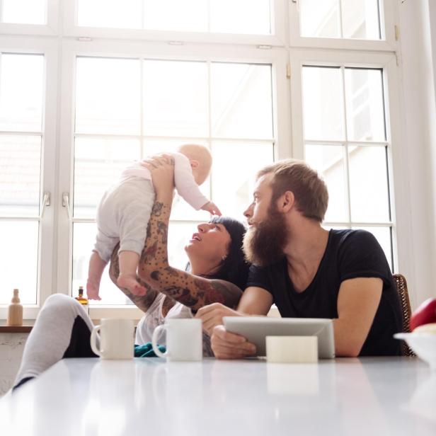 Eine junge Familie mit einem Neugeborenen am Tisch.