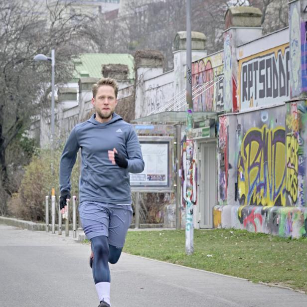 Ein Mann joggt auf einer Straße entlang einer mit Graffiti bemalten Mauer.