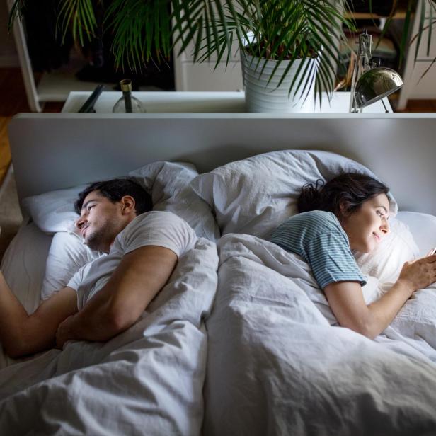 Ein Mann und eine Frau liegen Rücken an Rücken im Bett und benutzen ihre Mobiltelefone. Das Paar ignoriert sich und nutzt seine Smartphones.