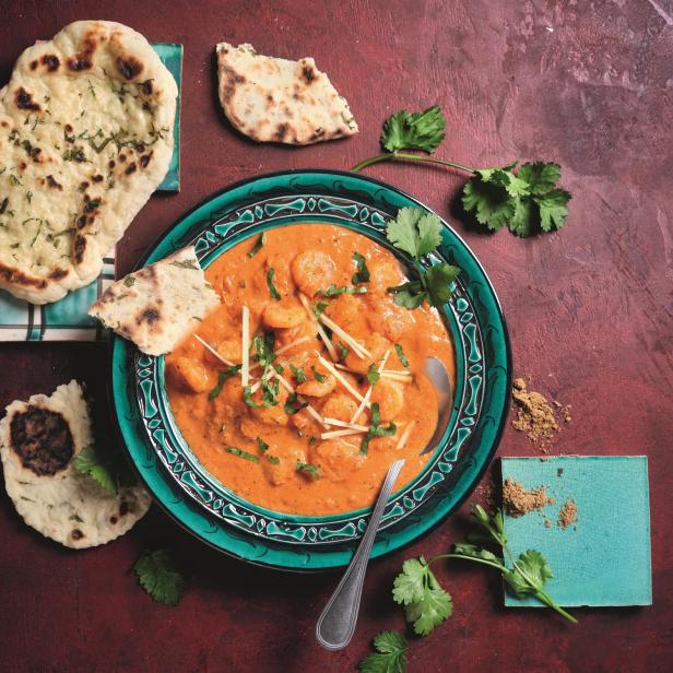Ein Teller mit Garnelen-Curry und Naan-Brot auf einem roten Untergrund.