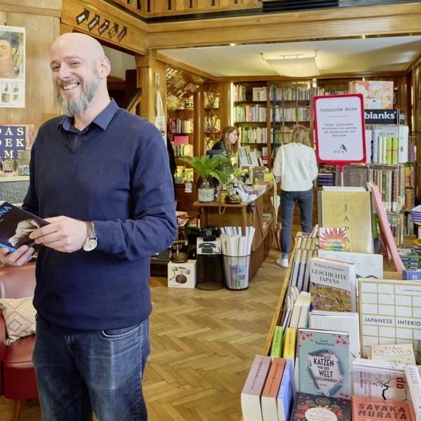 Ein Mann mit Buch steht in einem Buchladen mit japanischer Literatur.