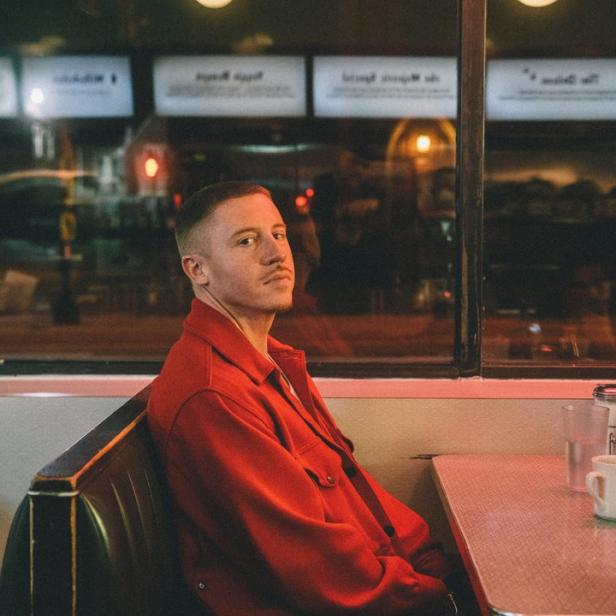 Macklemore sitzt in einem roten Anzug in einem Diner.