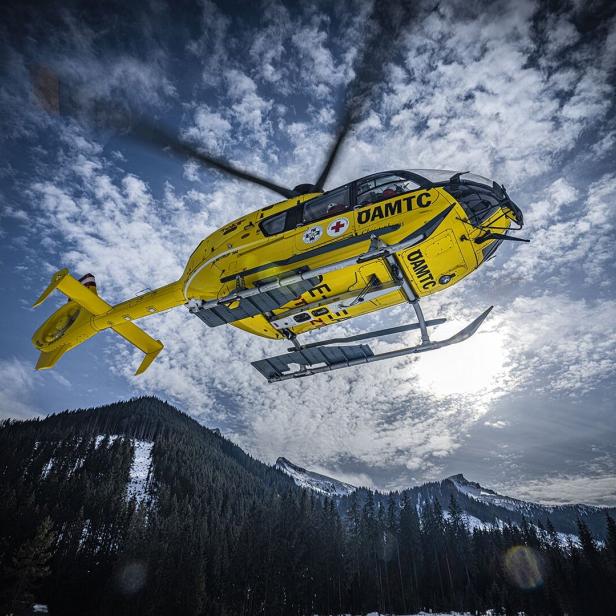 Ein gelber Rettungshubschrauber des ÖAMTC fliegt über eine verschneite Berglandschaft.