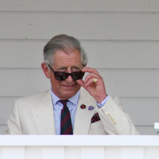 König Charles III. blickt über eine Brüstung und justiert seine Sonnenbrille.