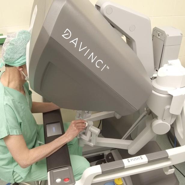 Ein Arzt in grüner OP-Kleidung bedient ein Da Vinci-Robotersystem.