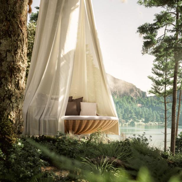 Ein hängendes Bett mit Baldachin hängt an einem Baum mit Blick auf einen See.