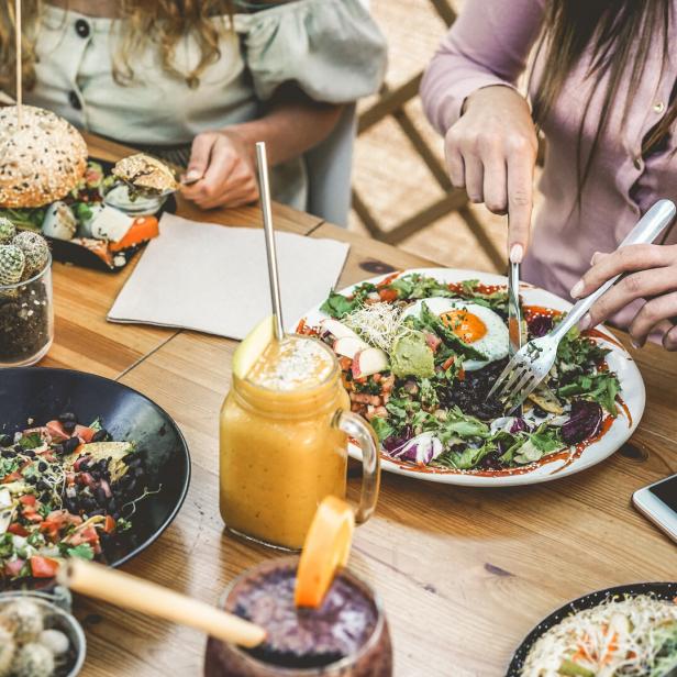 Junge Leute essen Brunch und trinken Smoothies in einem Restaurant ohne Plastik. Fokus auf den Teller mit Gabel.