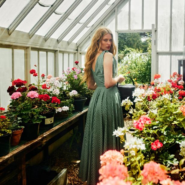 Eine Frau in einem grünen Kleid gießt in einem Gewächshaus Blumen.
