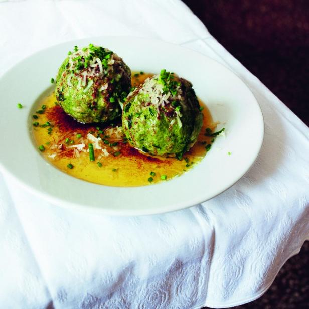 Zwei Spinatknödel liegen auf einem Teller mit zerlassener Butter und Parmesanraspeln.