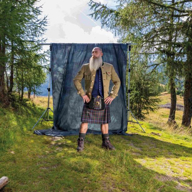 Ein Mann mit Bart und Kilt von Rettl 1868 posiert vor einem Hintergrund im Freien.