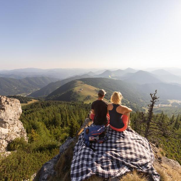 Ein Paar sitzt auf einer Decke auf einem Berggipfel und blickt in die Ferne.