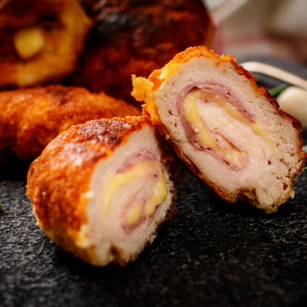Ein aufgeschnittenes, paniertes Cordon Bleu mit Schinken und Käsefüllung auf einem Teller.