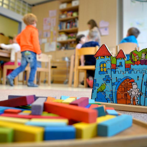 Kinder spielen mit einem Holzpuzzle und Bausteinen in einem Kindergarten.