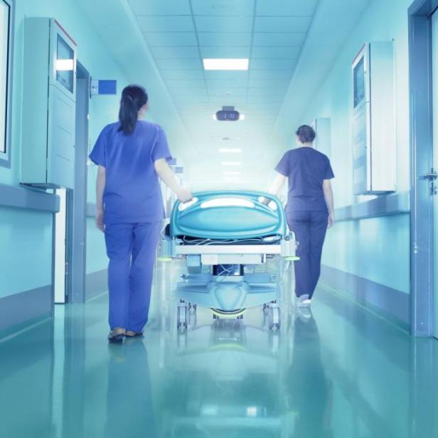 Zwei Krankenschwestern schieben eine leere Trage durch einen Krankenhausflur.