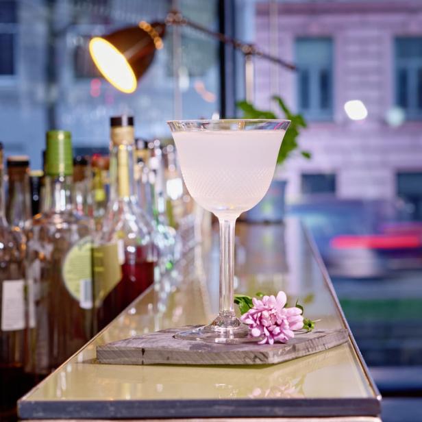 Ein Cocktail in einem eleganten Glas steht auf einer Bar, dekoriert mit einer rosa Blume.