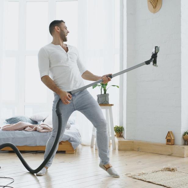 Young man having fun cleaning house with vacuum cleaner dancing like guitarist