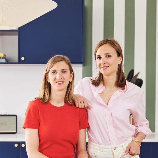 Zwei Frauen posieren in einem Raum mit blau gestreiften Wänden.