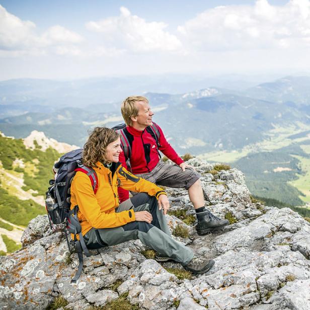Eine Frau und ein Mann sitzen auf einem Felsen und genießen die Aussicht auf einem Berg.