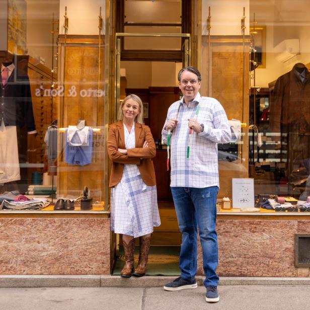 Ein Mann mit Maßband und eine Frau stehen vor dem Schaufenster eines Bekleidungsgeschäfts.