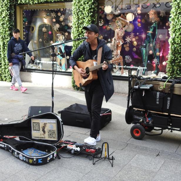 Ein Straßenmusiker spielt Gitarre vor einem Schaufenster.