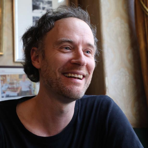 Ein lächelnder Mann mit Bart sitzt in einem Café.