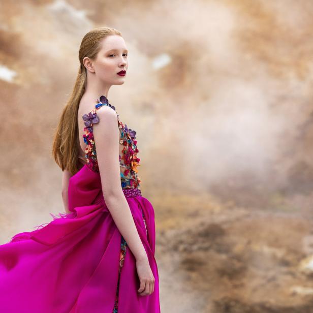 Eine Frau in einem pinkfarbenen Kleid mit Blumenapplikationen blickt über ihre Schulter.