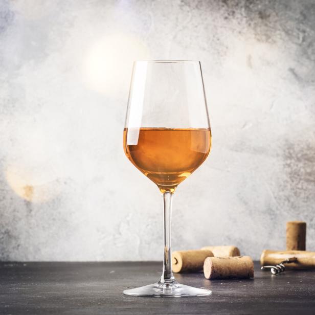 Ein Glas oranger Wein steht auf einem Tisch mit Weinkorken.