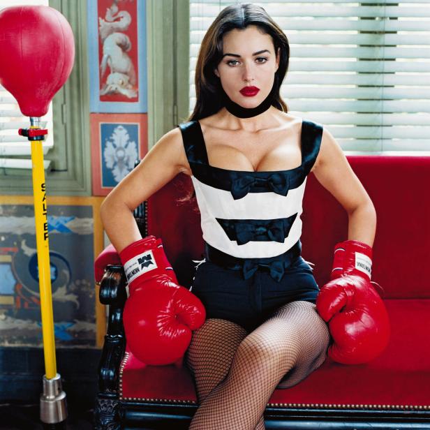 Monica Bellucci posiert mit Boxhandschuhen auf einem roten Sofa.