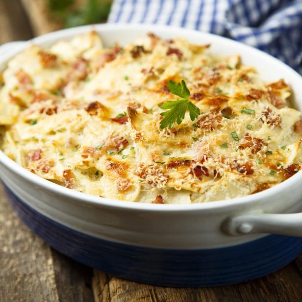 Ein Kartoffelgratin mit Käse und Speck in einer ovalen Auflaufform.