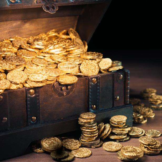 Eine geöffnete Schatztruhe ist mit Goldmünzen gefüllt.
