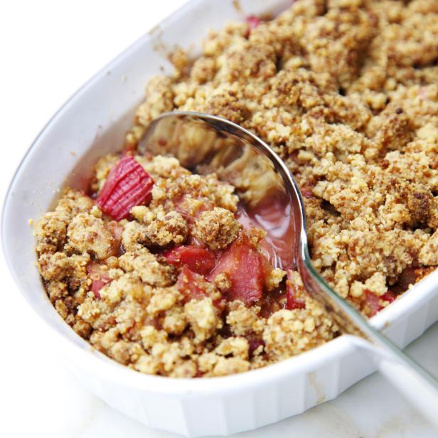 Ein Rhabarber-Crumble in einer weißen Auflaufform mit einem Löffel.