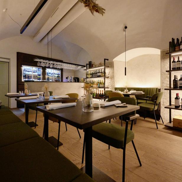 Innenansicht eines eleganten Restaurants mit gedeckten Tischen und Weinregalen.
