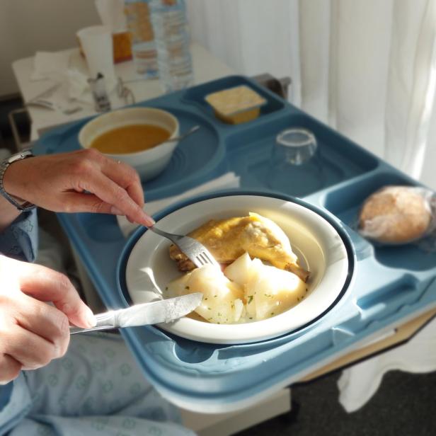 Eine Person isst im Krankenhaus Hähnchen und Kartoffeln.