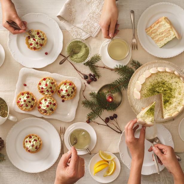 Ein Tisch mit Törtchen, Kuchen, Tee und weihnachtlicher Dekoration von oben fotografiert.