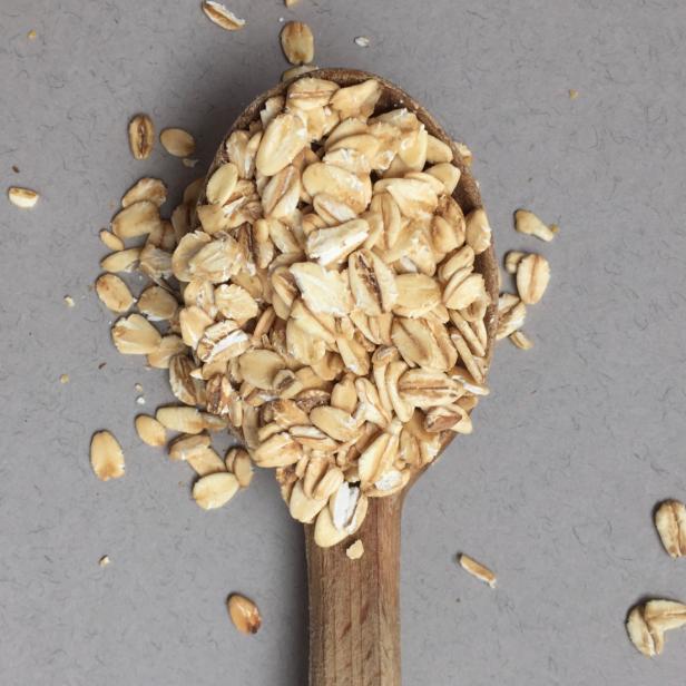 Ein Holzlöffel voller Haferflocken auf einem grauen Untergrund.