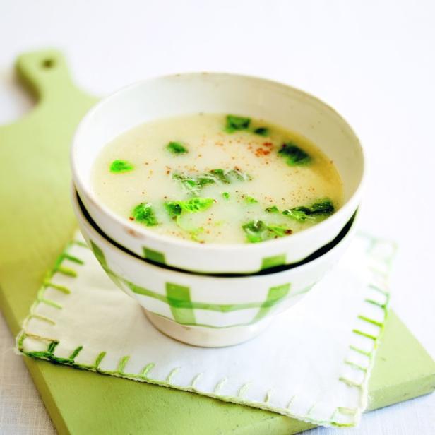 Eine Schüssel cremige Suppe mit grünen Kräutern auf einem grünen Schneidebrett.