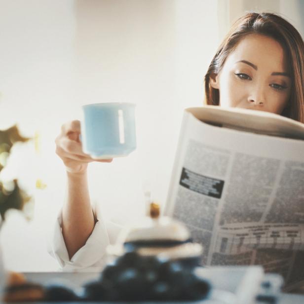 Eine Frau liest Zeitung und hält eine Tasse in der Hand.