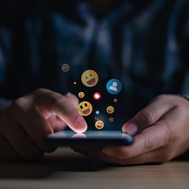 Ein junger Mann tippt auf sein Smartphone, wobei verschiedene positive Emojis auf dem Bildschirm erscheinen.