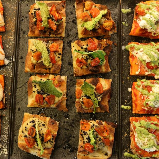 Verschiedene Pizzastücke mit unterschiedlichen Belägen auf einem schwarzen Blech.