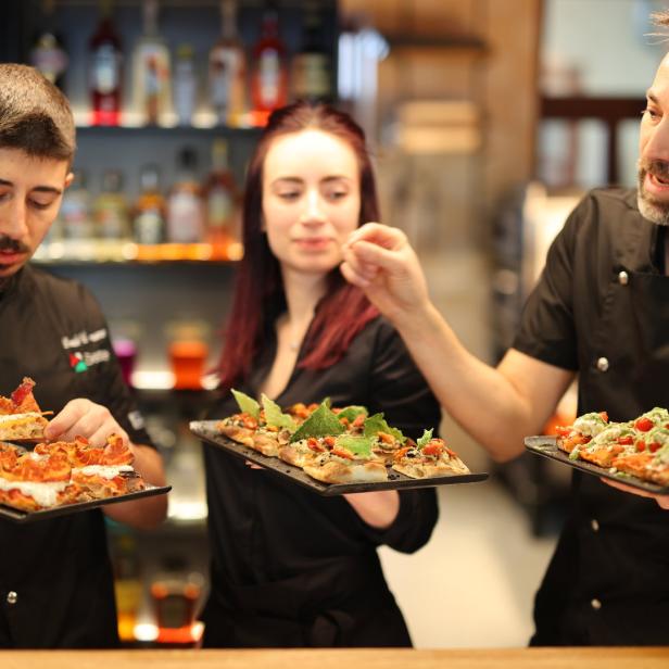 Drei Köche präsentieren verschiedene Sorten Pizza auf schwarzen Tellern.