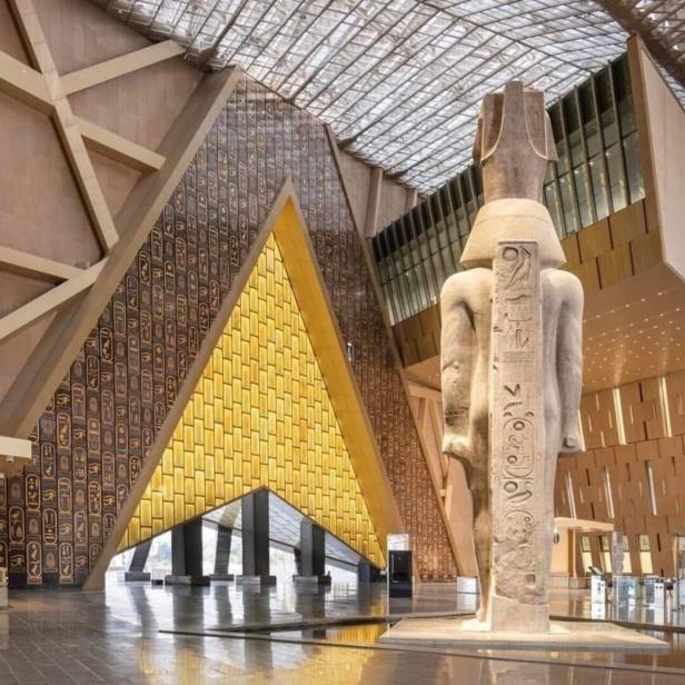 Innenansicht des Grand Egyptian Museum mit einer Statue und Hieroglyphen an den Wänden.