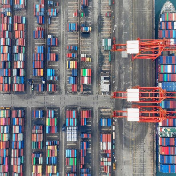 Luftaufnahme eines Containerschiffs im Hafen, beladen mit bunten Containern.
