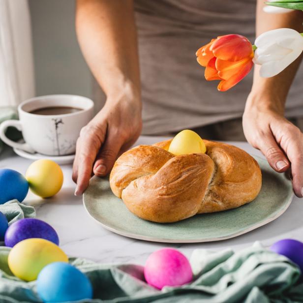 Ein Osterbrot mit einem gelben Ei wird von bunten Ostereiern und Tulpen umgeben.