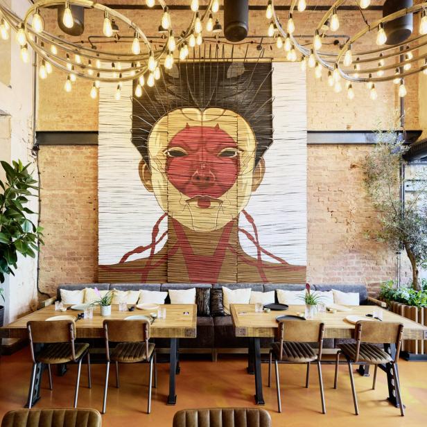 Ein Restaurant mit Holztischen, Stühlen und einem großen Wandbild einer Person.